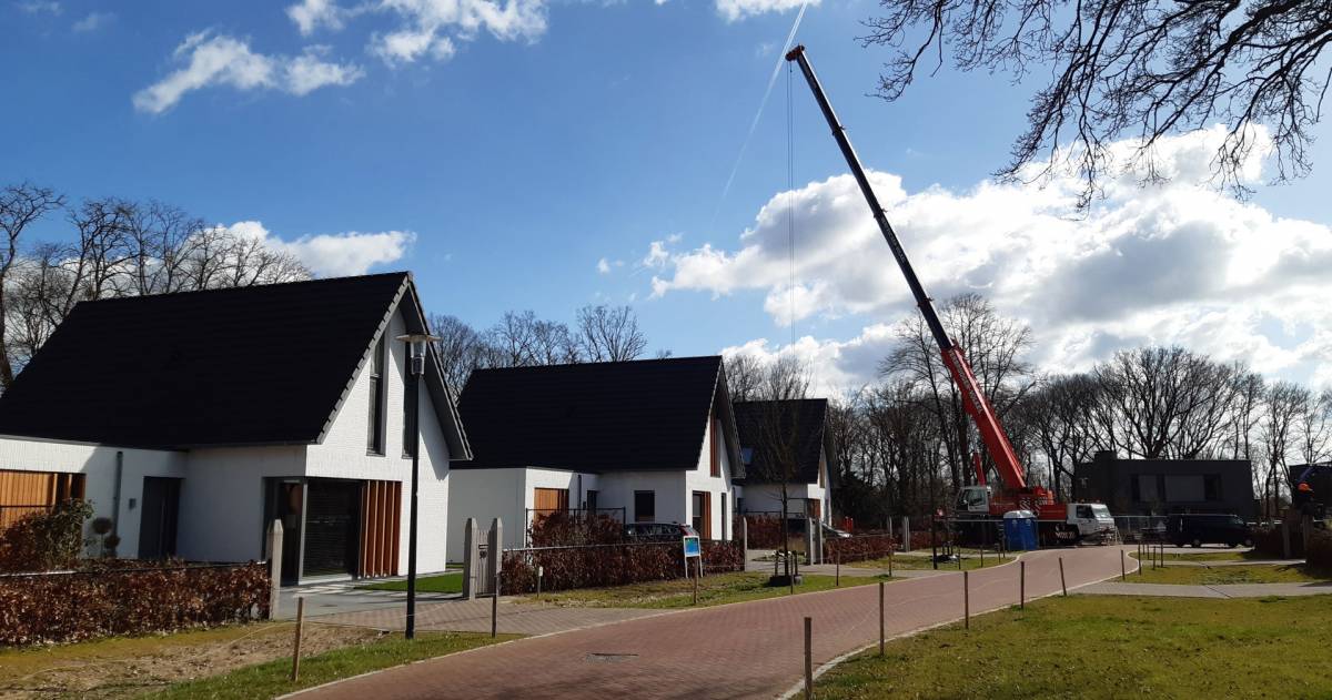 Een nieuwbouwproject met witten huizen en zwarte daken en een hijskraan op de achtergrond